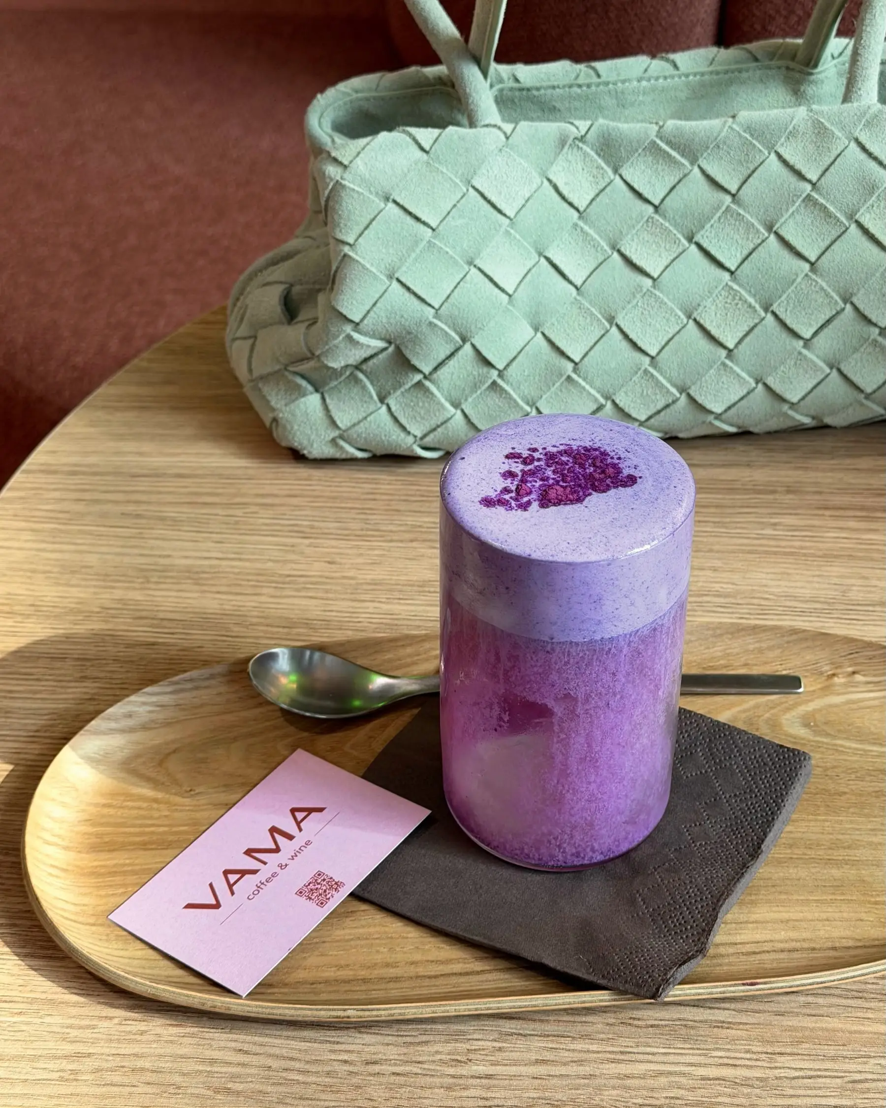 Lila Ube Latte auf einem Holztablett, daneben die rosa VAMA-Visitenkarte